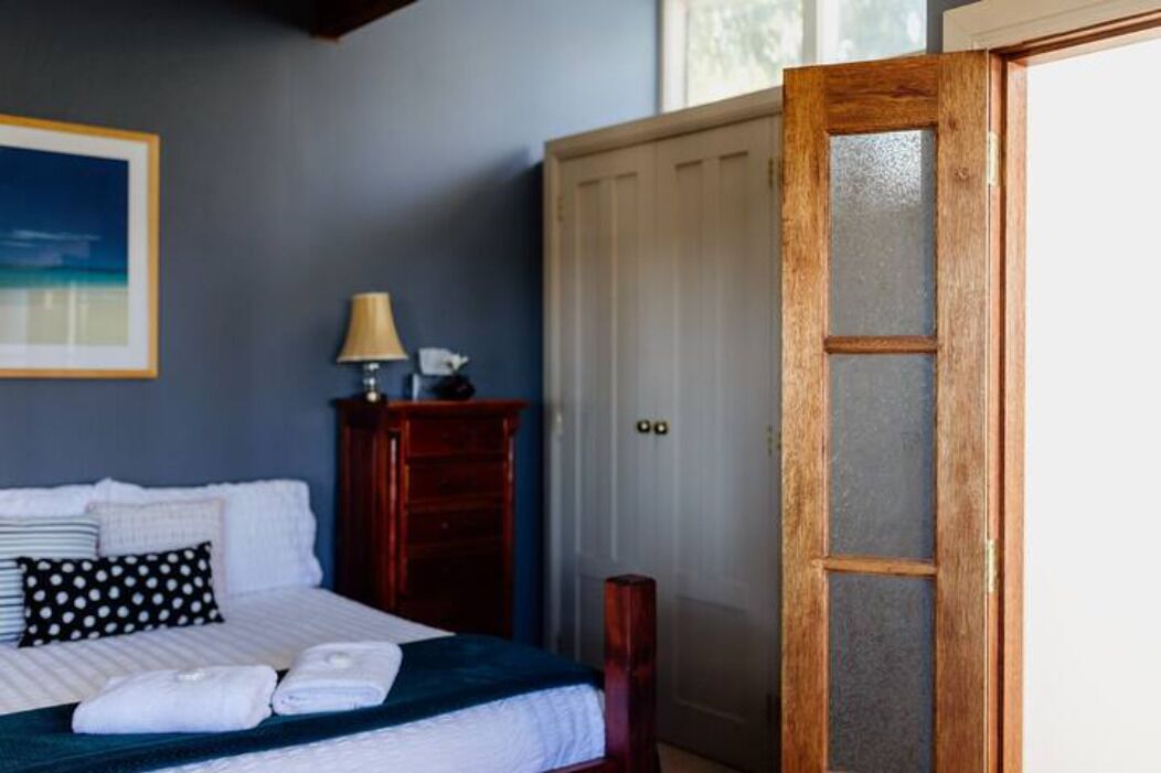 Un dormitorio con cama, almohadas, mesita de noche, lámpara, armario y puerta.