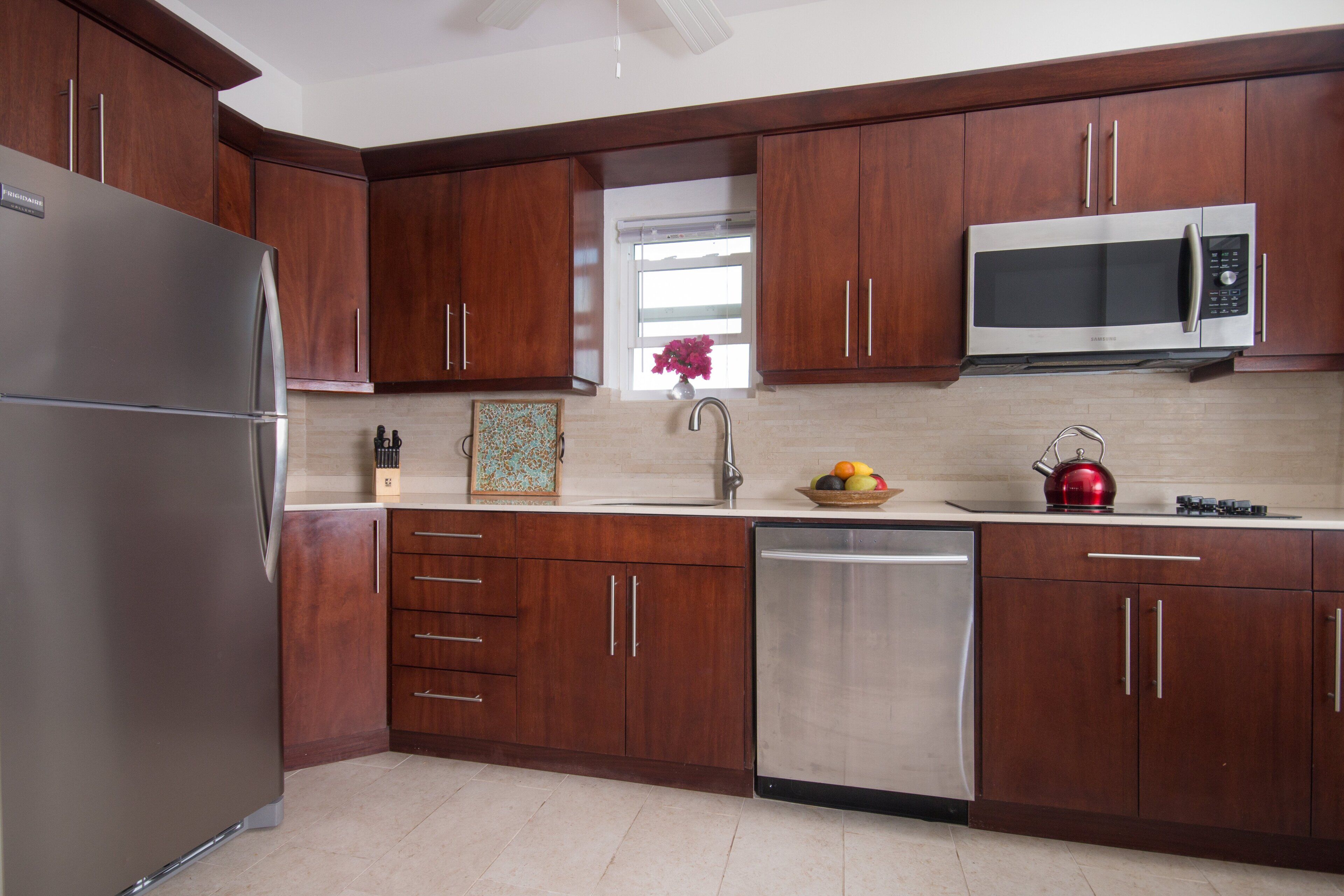 A modern kitchen with wooden cabinets, stainless steel appliances, and a window with a flower vase.