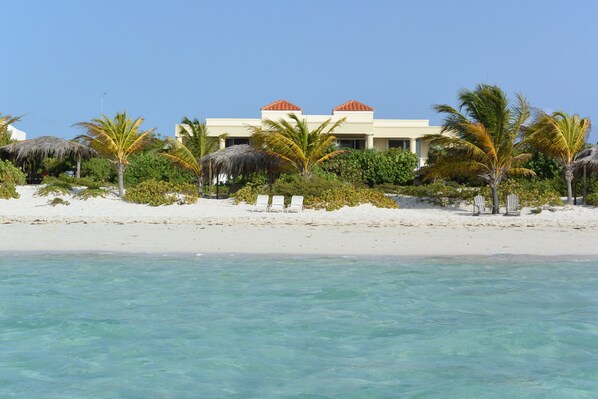 Ein Strandhotel mit weißem Gebäude, Palmen und klarem, türkisblauem Wasser.