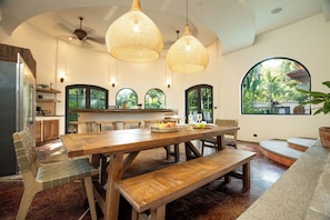 Une cuisine spacieuse avec une grande table en bois, des placards intĂ©grĂ©s en bois et une vue sur lâextĂ©rieur grĂące Ă de grandes fenĂȘtres en arc de cercle.