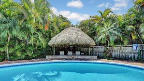 A swimming pool with a thatched-roof structure surrounded by lush tropical vegetation. - Delray Home W/Pool-Close To Beach & Downtown Atlantic Ave-Fun Tiki Hut-Bike-WiFi (Delray Beach)