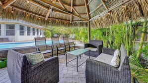 A covered outdoor area with wicker furniture, a pool, and lush greenery. - Delray Home W/Pool-Close To Beach & Downtown Atlantic Ave-Fun Tiki Hut-Bike-WiFi (Delray Beach)