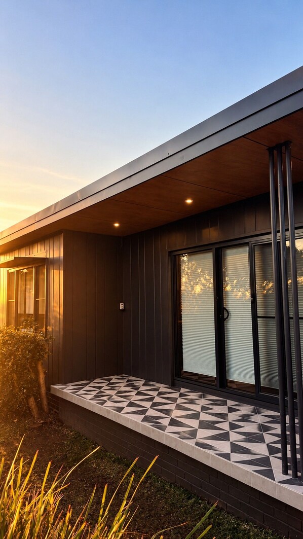A modern building with a flat roof, large sliding glass doors, and a geometric patterned tile floor. - Culburra Retreat - Newly Renovated, Pet Friendly, 4 Min Walk to the Beach (Culburra Beach)