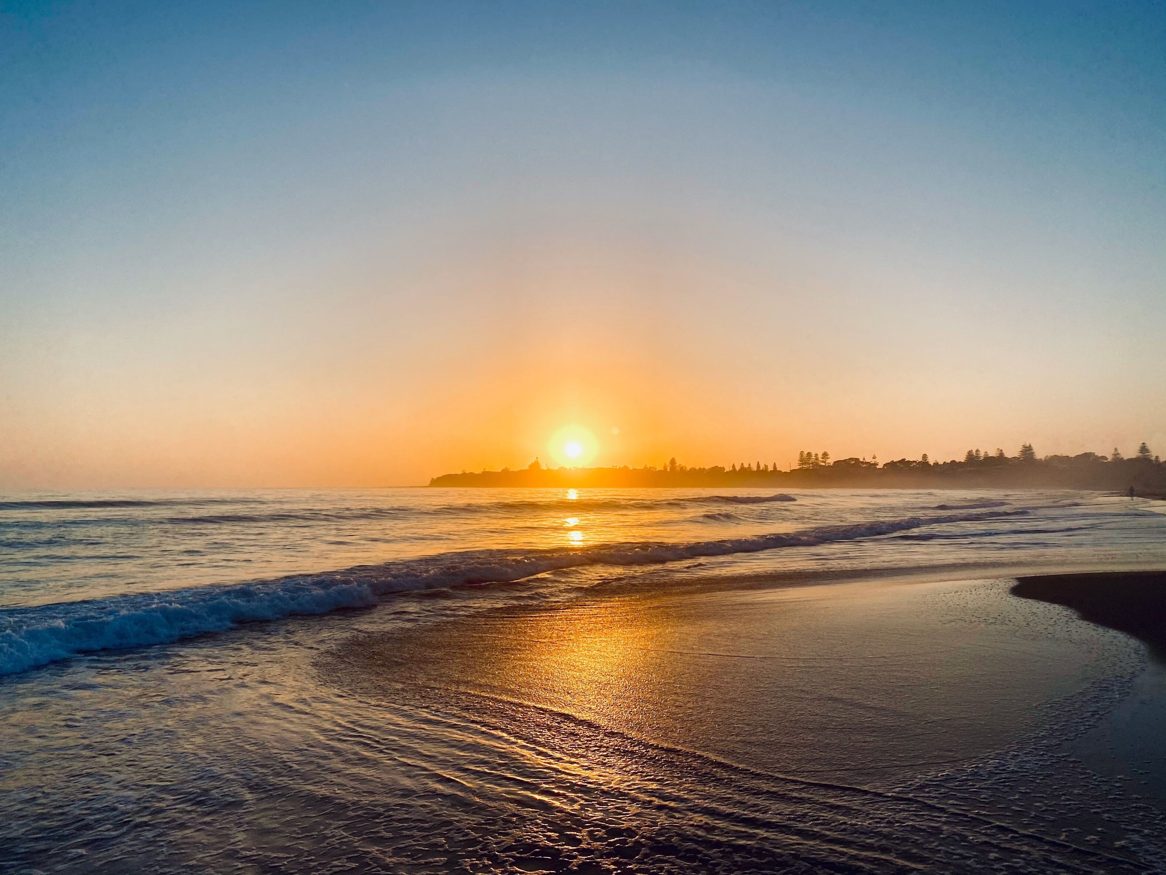 Une plage au coucher du soleil, où les vagues viennent doucement lécher le rivage.