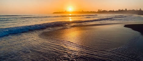 Une plage au coucher du soleil, où les vagues viennent doucement lécher le rivage.