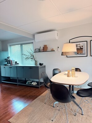 A compact kitchen with a dining area, featuring a round table, black chairs, and a small rug. - Culburra Retreat - Newly Renovated, Pet Friendly, 4 Min Walk to the Beach (Culburra Beach)