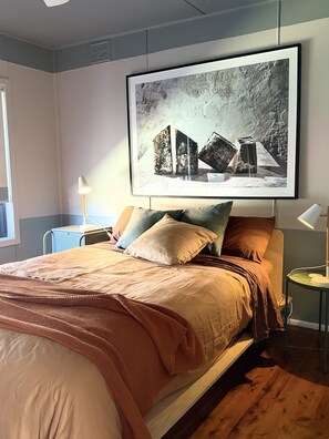 Une chambre à coucher avec un lit, des oreillers, un tableau encadré au mur, une table de chevet et une lampe.
