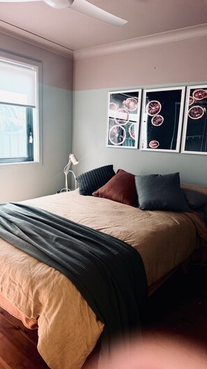 A bedroom with a bed, pillows, a bedside table, a lamp, and wall art. - Culburra Retreat - Newly Renovated, Pet Friendly, 4 Min Walk to the Beach (Culburra Beach)
