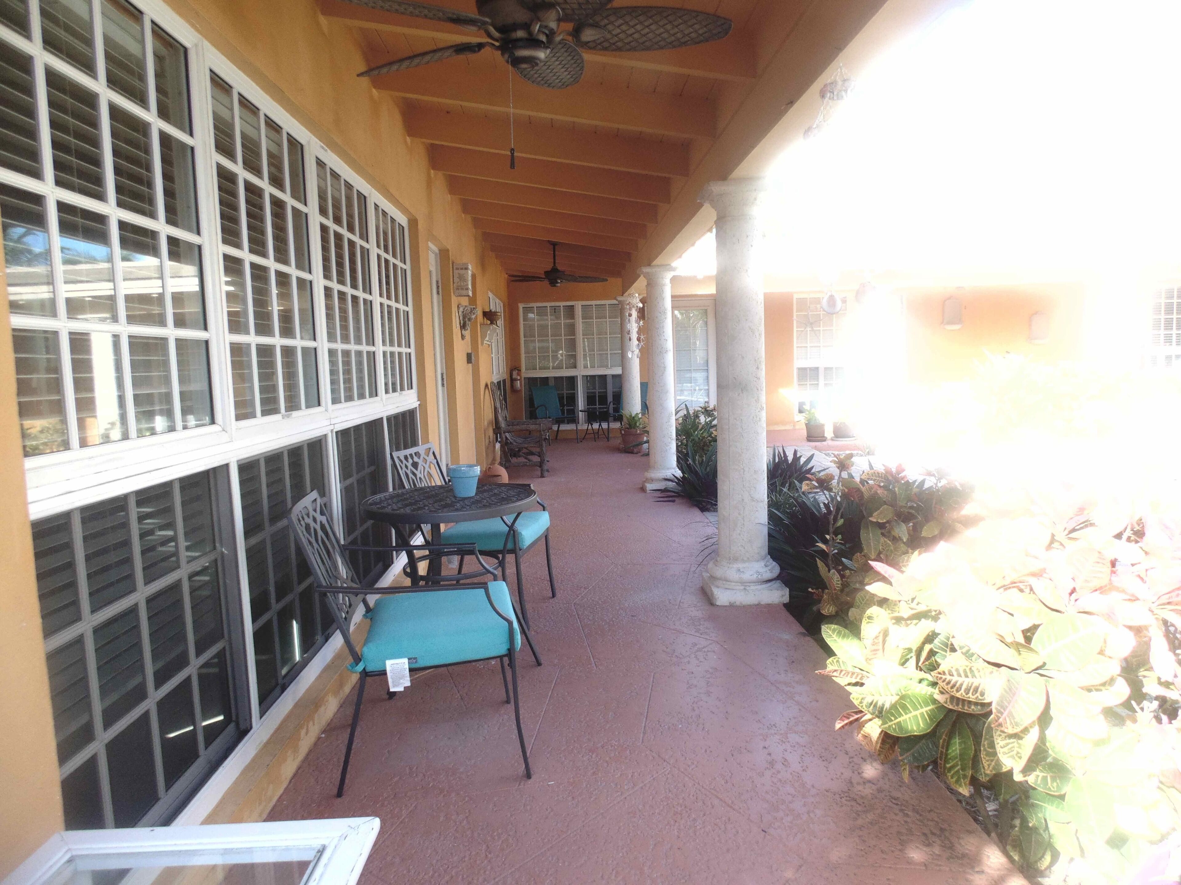 A covered patio with a table and chairs, large windows, and a ceiling fan.