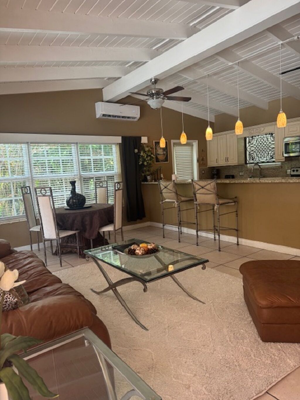 A living room with a glass coffee table, brown leather sofa, and a dining area with a table and chairs.