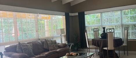 A spacious living room with a brown leather sofa, a glass coffee table, and a dining area with a table and chairs.