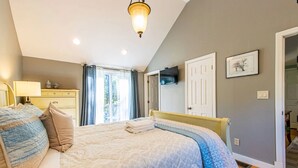 A bedroom with a bed, bedside table, lamp, and a view of the outside through a window.