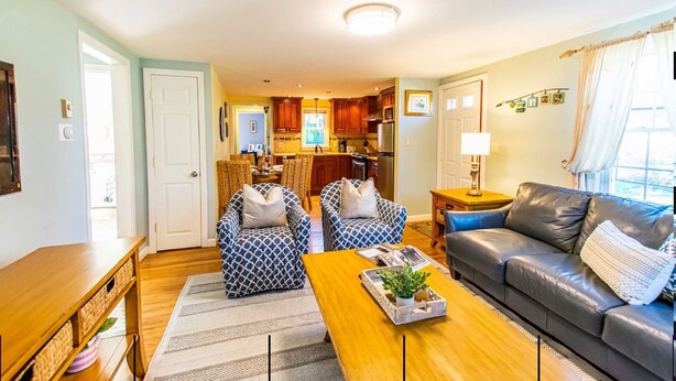 A living room with a sofa, two patterned armchairs, a wooden coffee table, and a kitchen in the background.