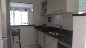 A kitchen with white cabinets, a black countertop, a sink, and a window with curtains. - Apartment in Cabo Frio, completely renovated, new furniture, bright, spacious, airy, quiet. (Cabo Frio)