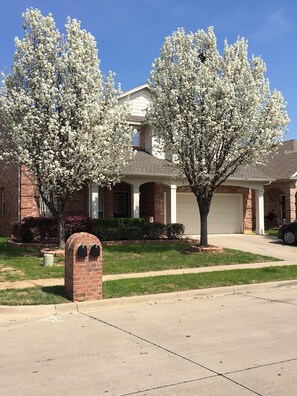 Stunning home with a brick facade, front porch, and two-car garage, set amidst a beautifully manicured lawn.