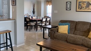 Amplia sala de estar con sofá marrón, una mesa de centro de madera y un comedor con sillas y una mesa.