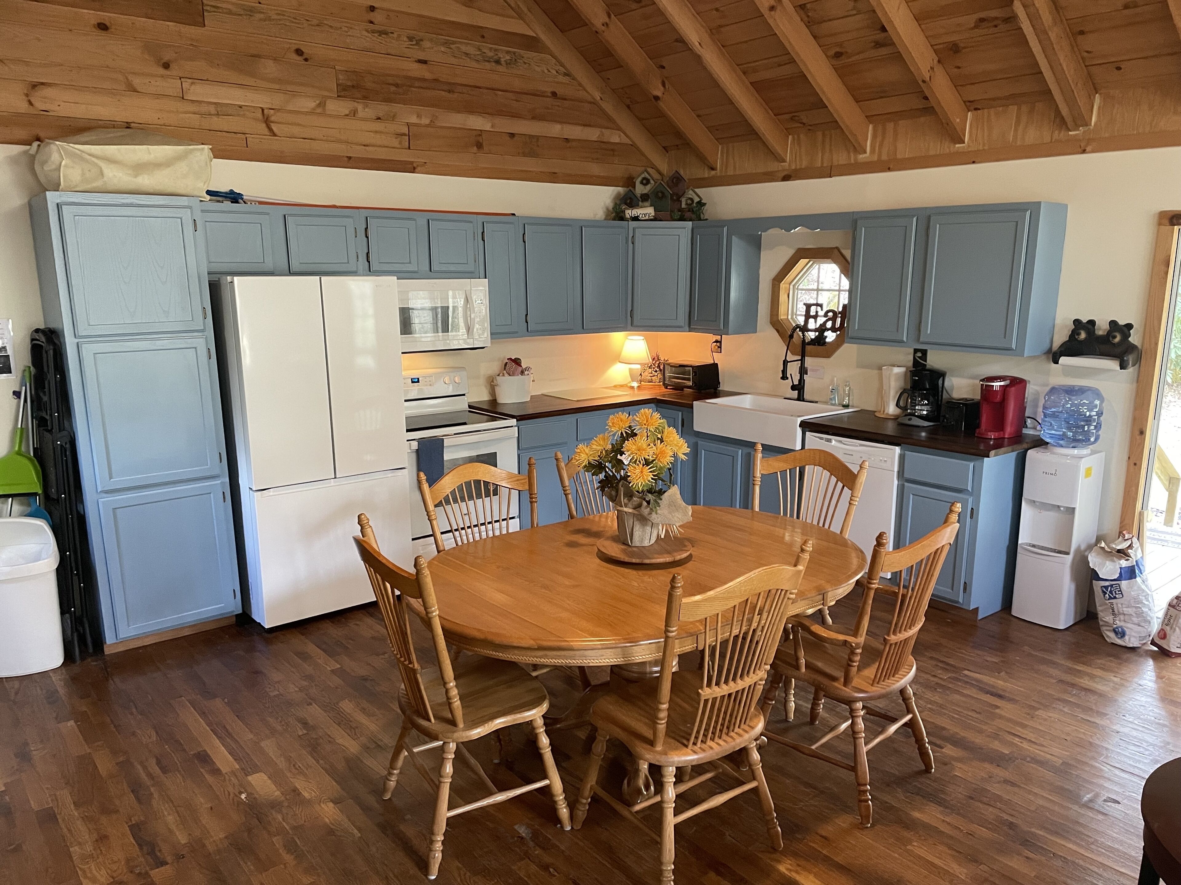 Une cuisine avec des meubles de rangement bleus, une table à manger en bois avec des chaises, un réfrigérateur, une cuisinière et un évier.
