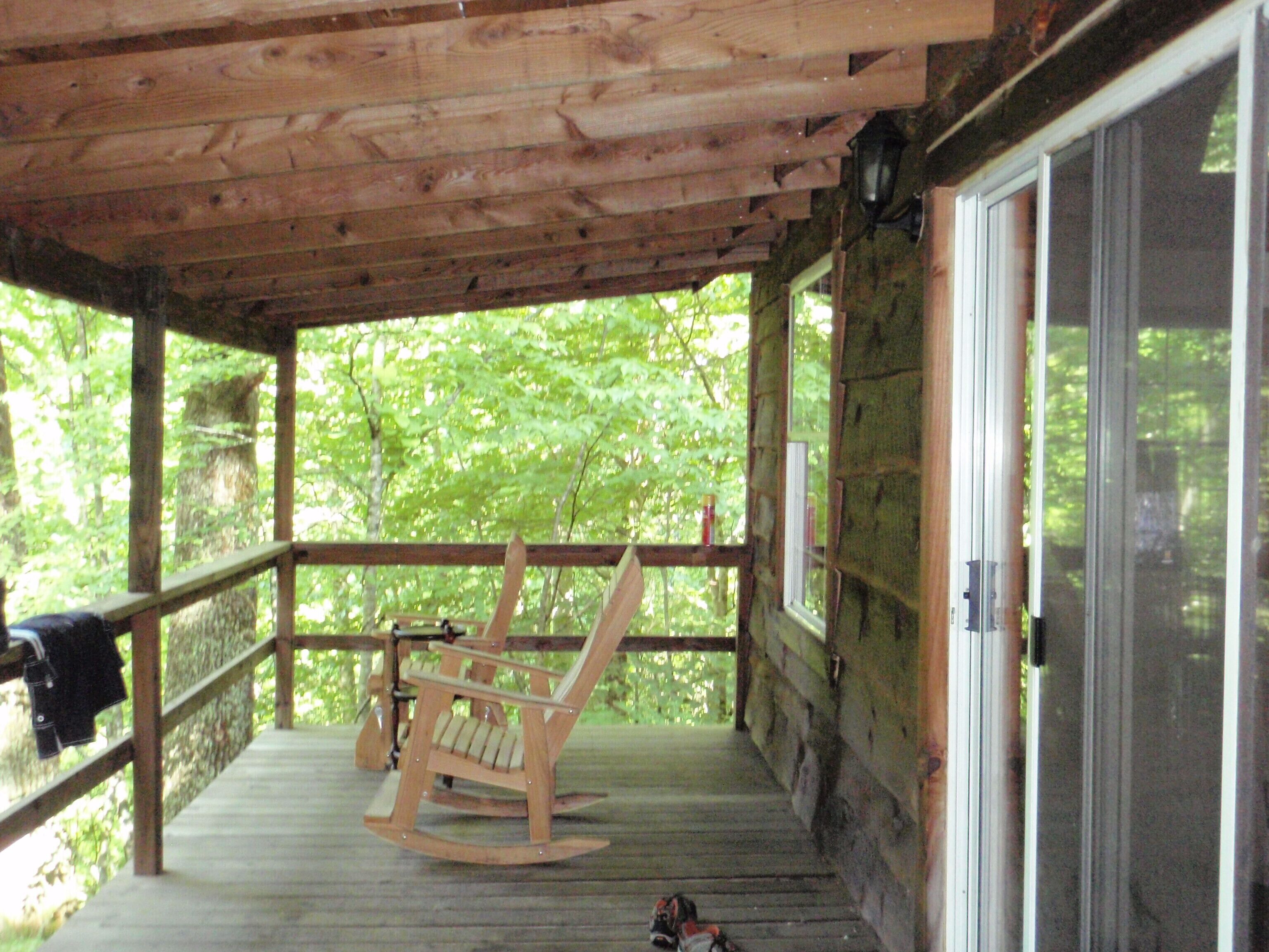 Une véranda en bois avec une chaise berçante et un barbecue.