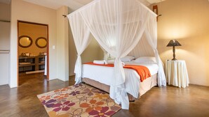 A bedroom with a four-poster bed, a bedside table with a lamp, and a floral rug. - vcvcbbvvbbvb (Hoedspruit)