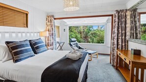 A bedroom with a bed, a chair, a desk, and a view of greenery outside. - Coromandel Cottage  - Romantic Rustic - Sea views (Coromandel Township)