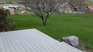 A wooden deck with a view of a rural landscape, including a tree and distant buildings. - The Dayton Lake Place (Dayton)