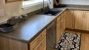 A kitchen with wooden cabinets, a stainless steel sink, and a black and white patterned rug. - The Dayton Lake Place (Dayton)