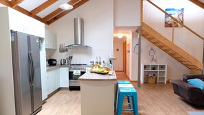 Une cuisine moderne dotée d’un îlot central, d’un four encastré et d’un réfrigérateur en acier inoxydable. Un escalier en bois mène à l’étage supérieur.