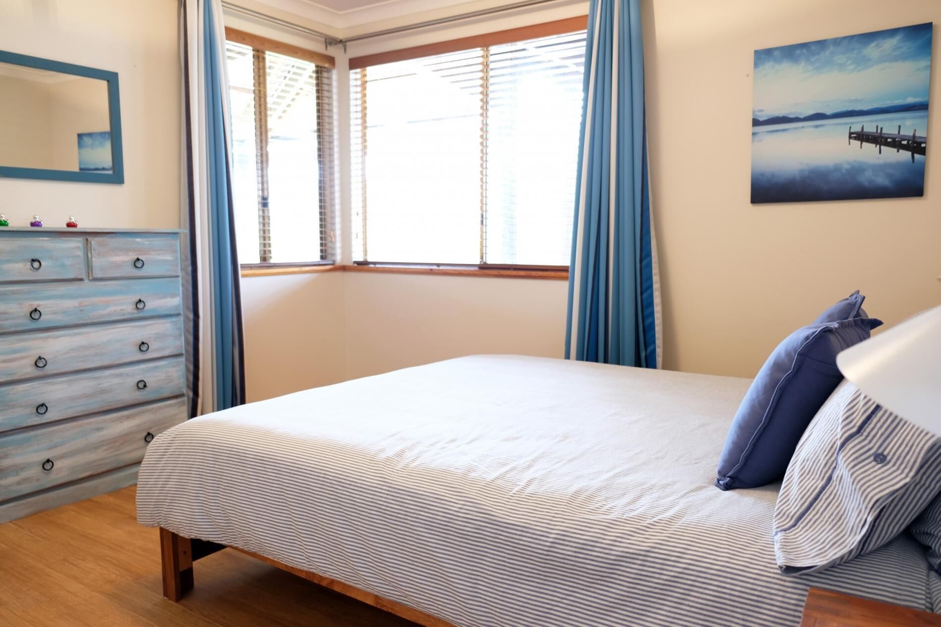 Een slaapkamer met een bed, een dressoir, een raam met gordijnen en een schilderij aan de muur.