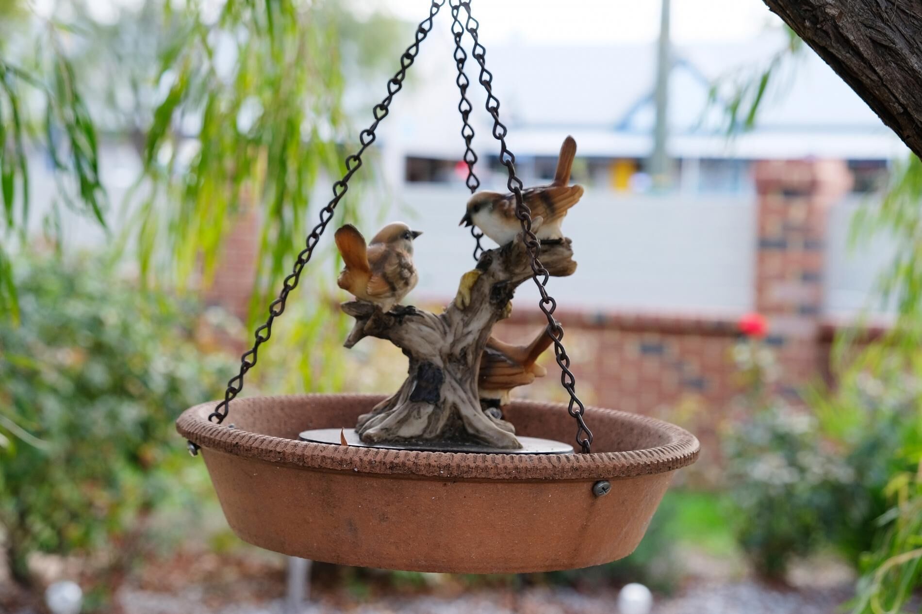 Une mangeoire à oiseaux suspendue, au design rustique, maintenue par des chaînes.