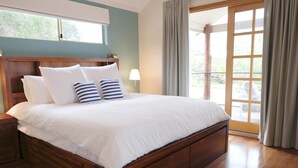 Un grand lit avec une literie blanche et des oreillers à rayures, une tête de lit en bois et une vue sur un balcon à travers une porte vitrée.