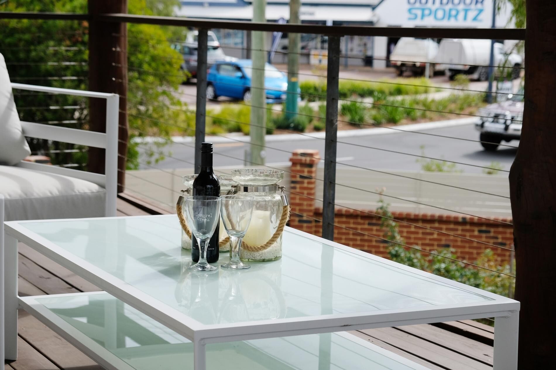 A glass-top table with a bottle and glasses on a balcony.
