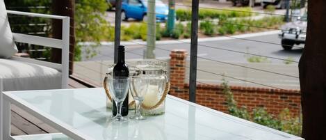 A glass-top table with a bottle and glasses on a balcony.