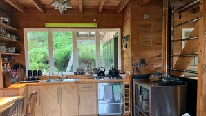 Cocina de cabaña de madera con un ventanal grande, armarios de madera, un fregadero, una estufa y un refrigerador.