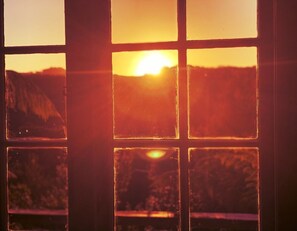 Una ventana con vista a un atardecer sobre un paisaje montañoso.
