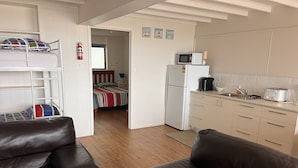 Ett kompakt bostadsutrymme med ett litet kök, en säng med ett färgglatt randigt överkast och en brun lädersoffa.