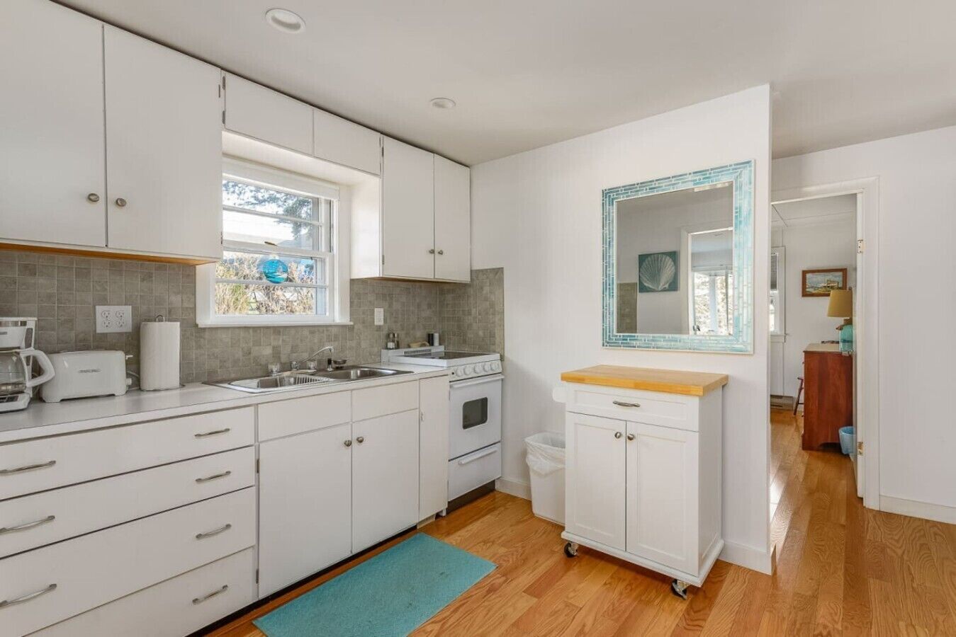 A modern kitchen with white cabinets, a built-in oven, a sink, and a window.