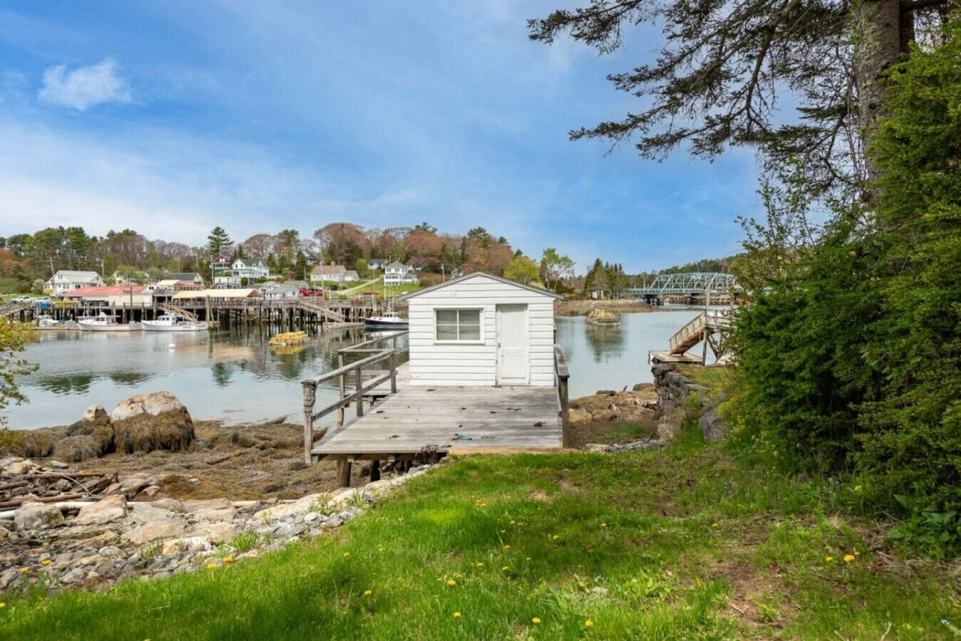 Un quai avec un petit bâtiment blanc, une passerelle en bois et des bateaux en arrière-plan.