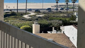 A balcony overlooking a beach with palm trees, a road with cars, and a clear sky. - Quiet Beautiful Beach Condo steps to beach, We are the best deal! (Port Hueneme)