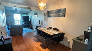 A spacious living area with a wooden floor, a dining table with chairs, a chandelier, and a large painting on the wall. - Quiet Beautiful Beach Condo steps to beach, We are the best deal! (Port Hueneme)