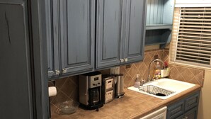 A kitchen with dark blue cabinets, a coffee maker, a dishwasher, and a window with blinds. - Quiet Beautiful Beach Condo steps to beach, We are the best deal! (Port Hueneme)