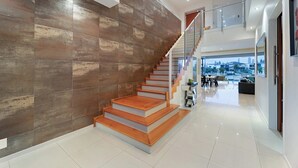 A modern interior with a wooden staircase, a glass railing, and a view of a cityscape through large windows. - Relaxed waterfront living (Gold Coast)