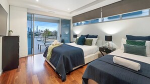 A modern hotel room with two beds, a balcony with a city view, and a desk with a lamp. - Relaxed waterfront living (Gold Coast)