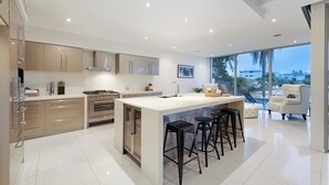 A modern kitchen with a central island, stainless steel appliances, and a large window offering a view of the city. - Relaxed waterfront living (Gold Coast)