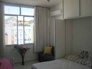 Quarto com cama, cadeira, mesa e janela.