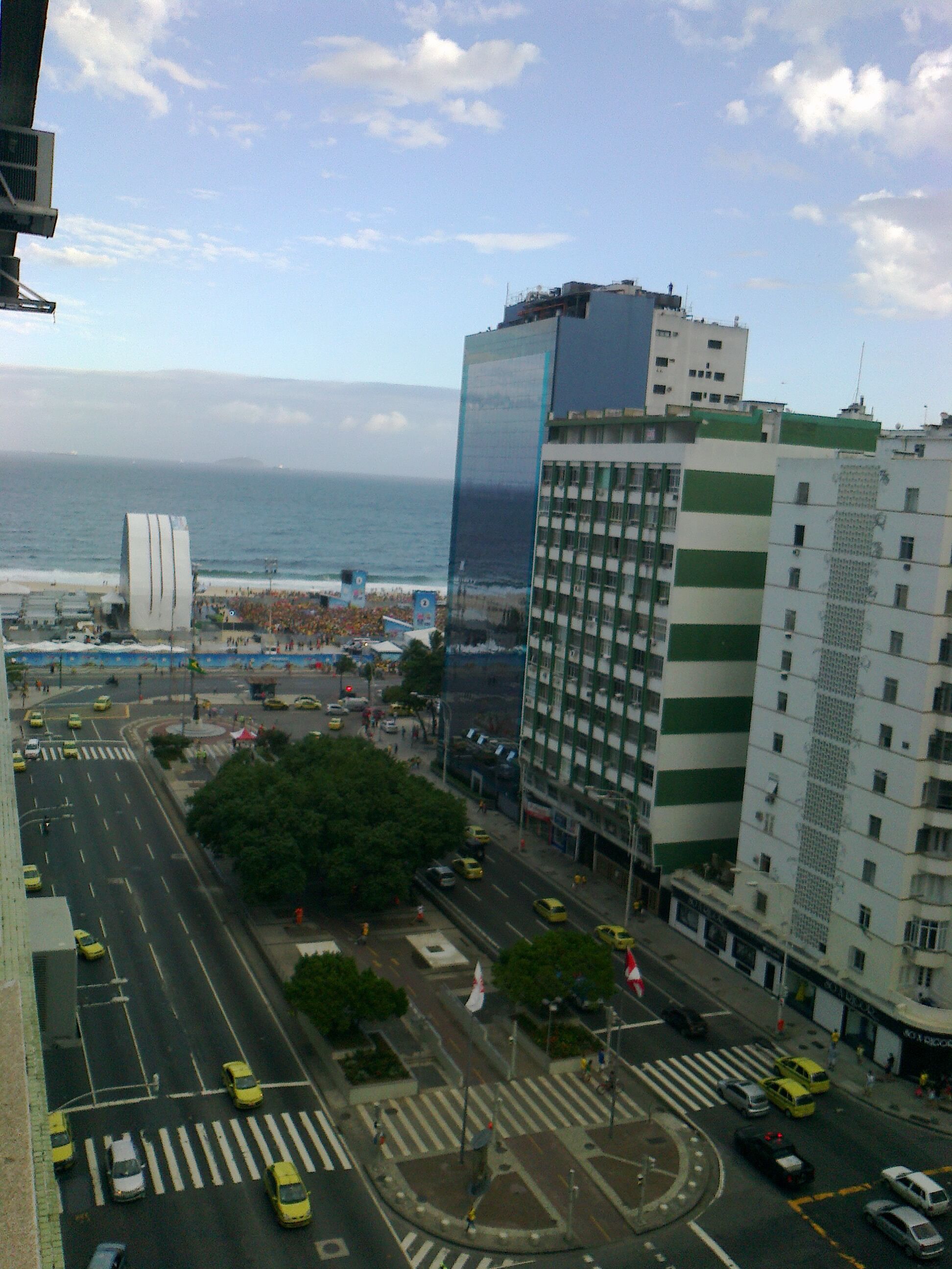 Eine Stadtansicht mit Blick auf das Meer, mit modernen Gebäuden, einer Fußgängerzone und einer belebten Straße mit gelben Taxis.