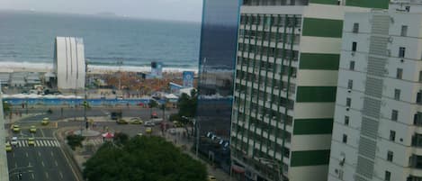 A cityscape with a view of the ocean, featuring modern buildings, a pedestrian crossing, and a busy street with yellow taxis.