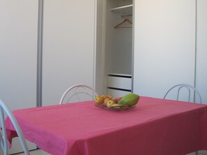 Um quarto com uma mesa rosa, uma cadeira e uma fruteira com bananas e maçãs.
