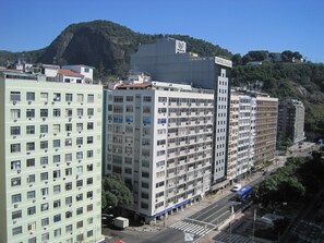 Um hotel com vários andares, uma placa de destaque, uma rua na frente e uma montanha ao fundo.