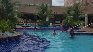 Área de piscina com várias piscinas, palmeiras e um edifício alto ao fundo.