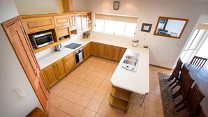 A kitchen with wooden cabinets, a microwave, a sink, and a dining area with chairs and a table. - Limestone Ridge River Getaway (Tailem Bend)
